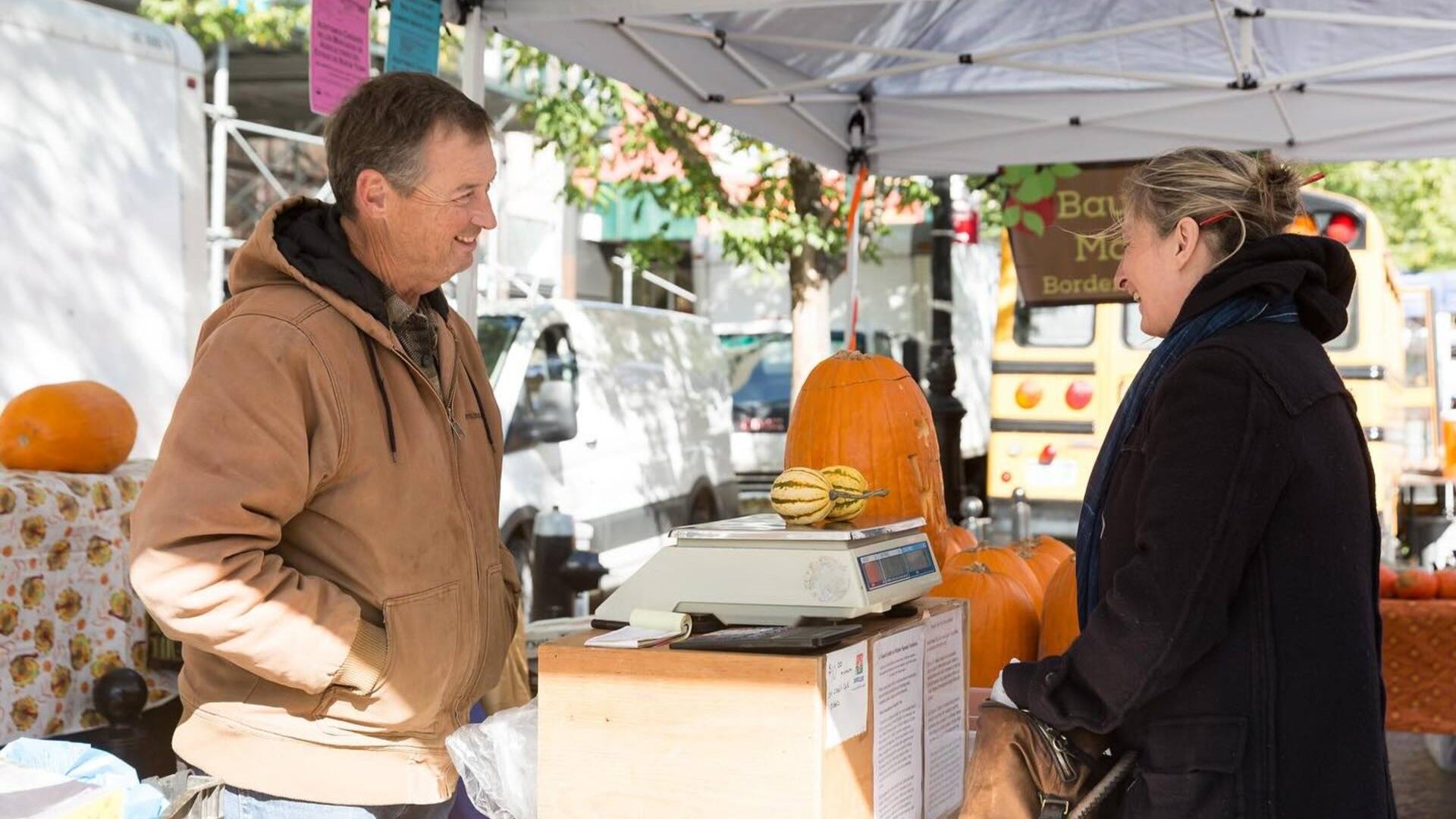 vendor and customer at a farmers market weighing produce